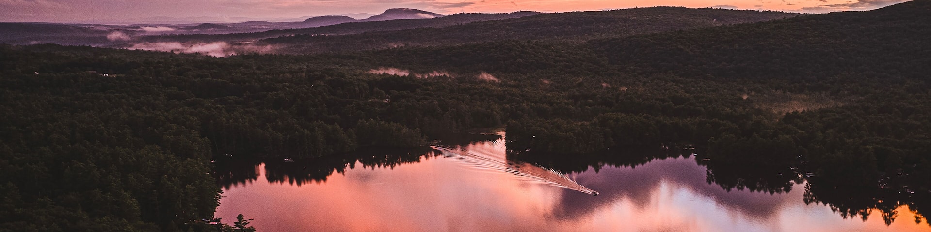 Vibrant sunset over smooth lake with boat. Range Pond, Poland, Maine