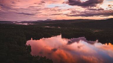 Vibrant sunset over smooth lake with boat. Range Pond, Poland, Maine