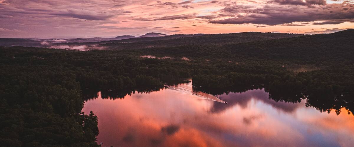 A lake surrounded by forested hills during sunset.