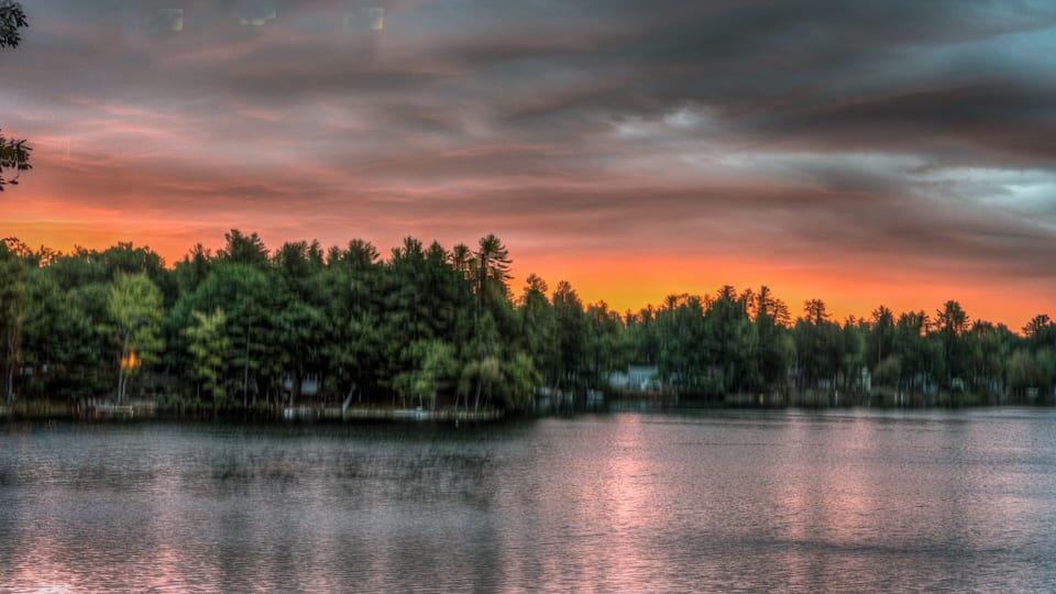 A lake at sunset with a forested shoreline and a cloudy sky.