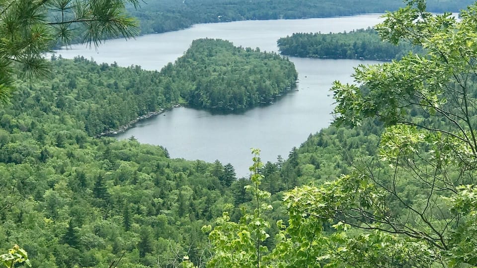 A lake surrounded by dense forest and a rocky outcrop in the foreground.