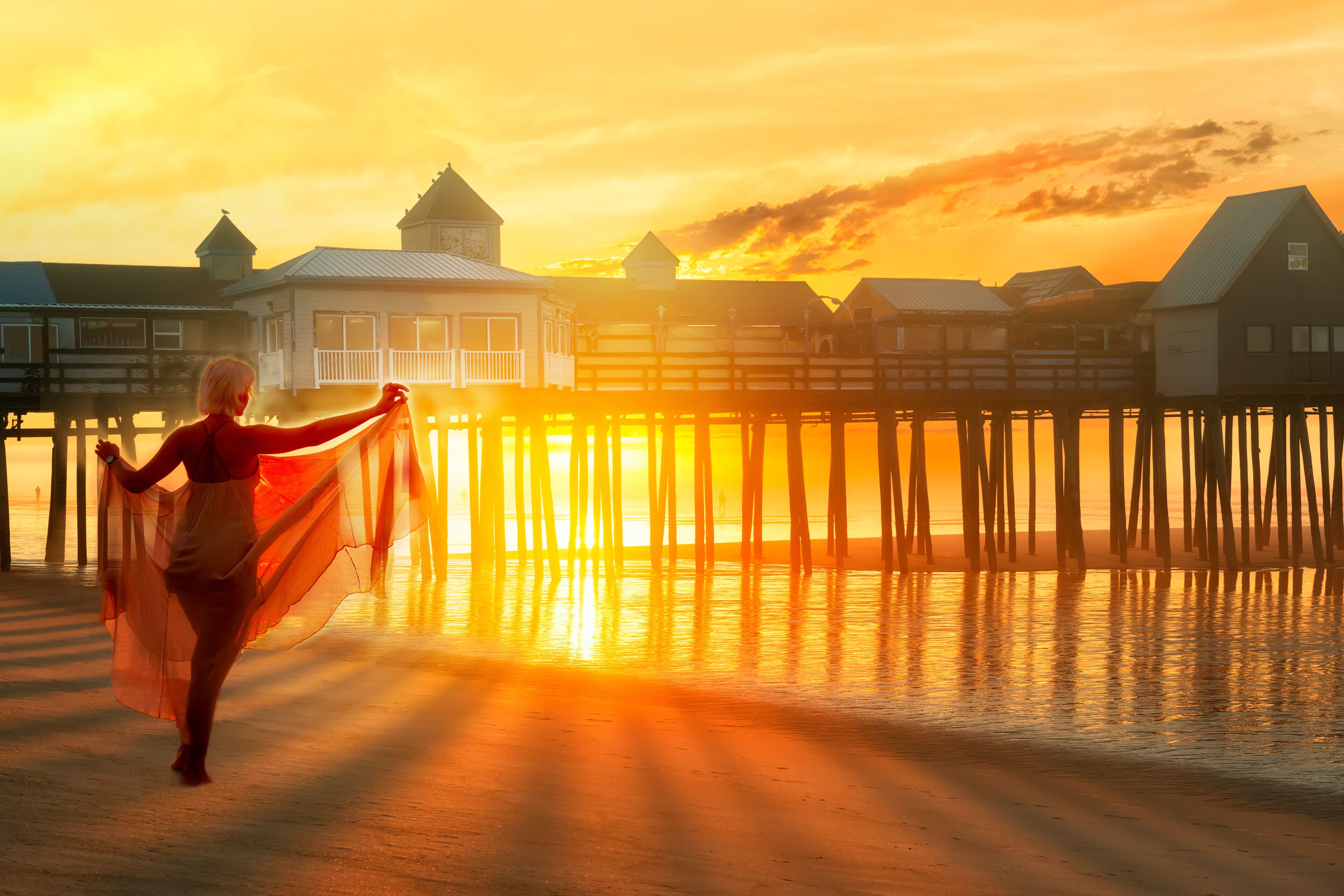 Un atardecer sobre un muelle con edificios y una persona con un vestido suelto.