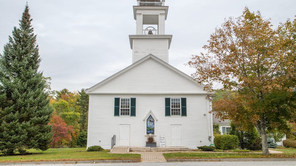 A white church with a steeple, green shutters, and a stained glass window.