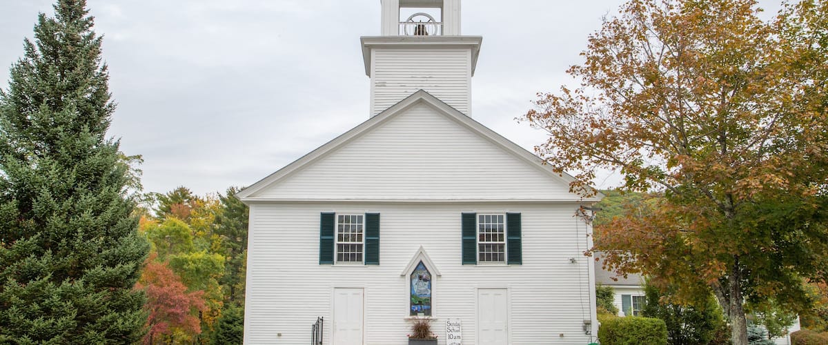 A white church with a steeple, green shutters, and a stained glass window.