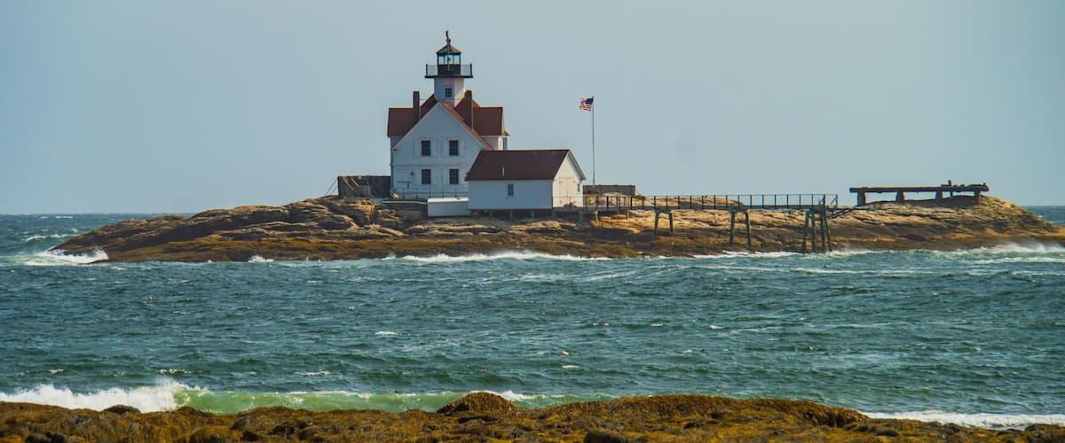 A lighthouse on a rocky island with waves crashing against it.