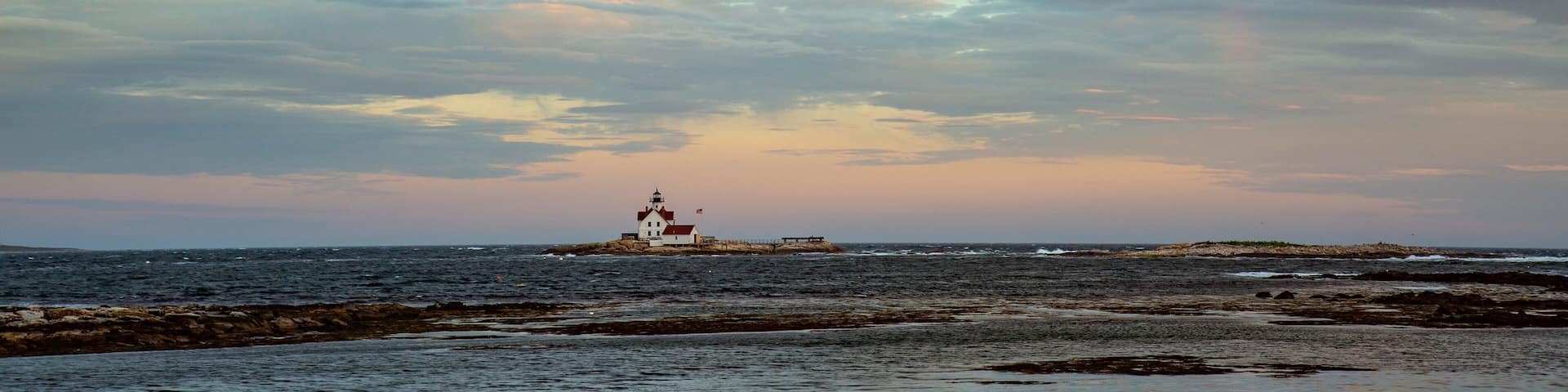 A lighthouse on a rocky outcrop with a rainbow in the sky.