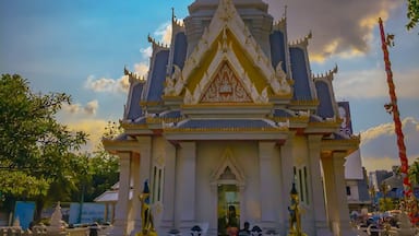 Un temple thaïlandais traditionnel, doté d’une flèche pointue, de décorations élaborées et surplombant un ciel dégagé où le soleil est visible.