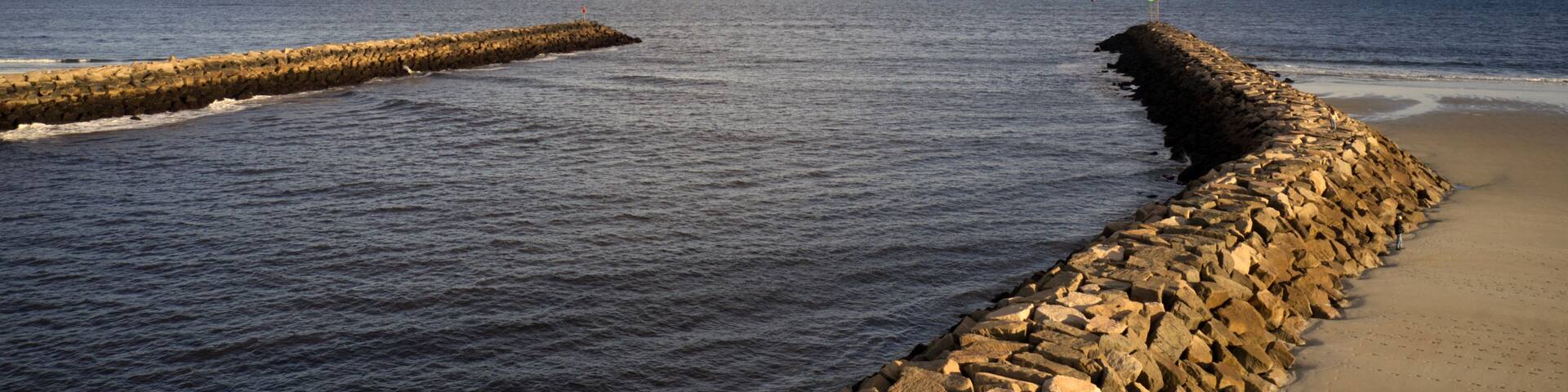 A rocky breakwater extending into the sea with a sandy beach on the right.