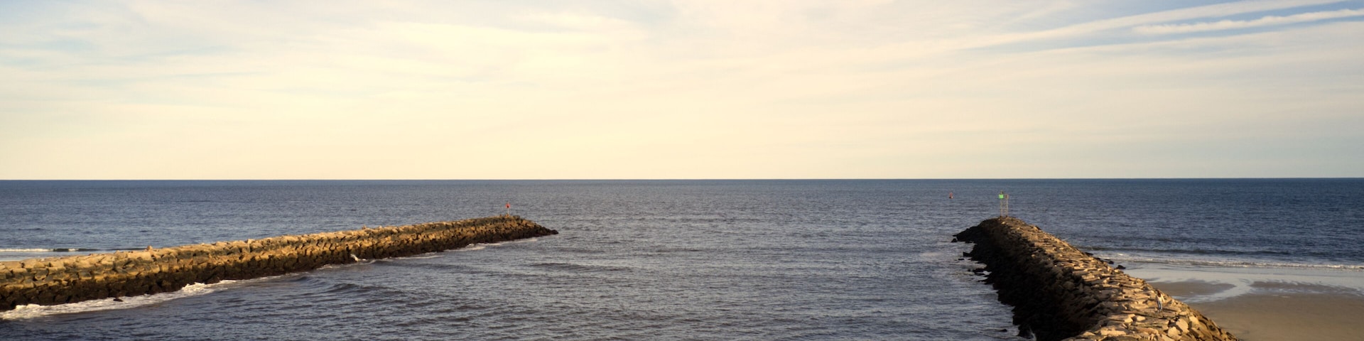 En stenet bølgebryder, der strækker sig ud i havet, med en sandstrand til højre.