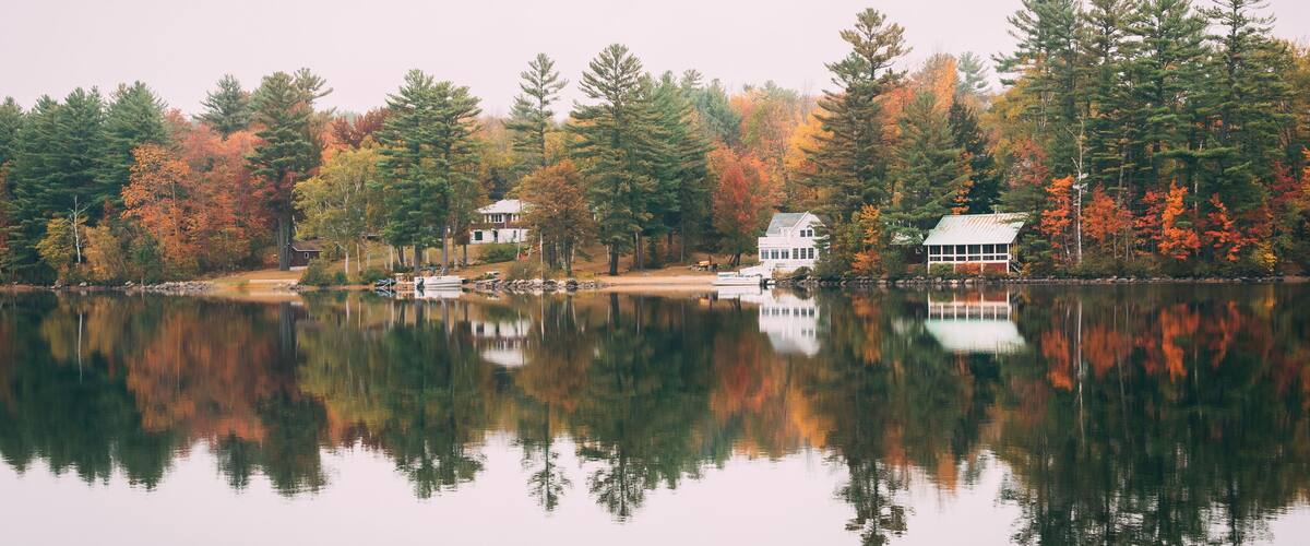 A calm lake with autumn-colored trees and two white houses on the shore.