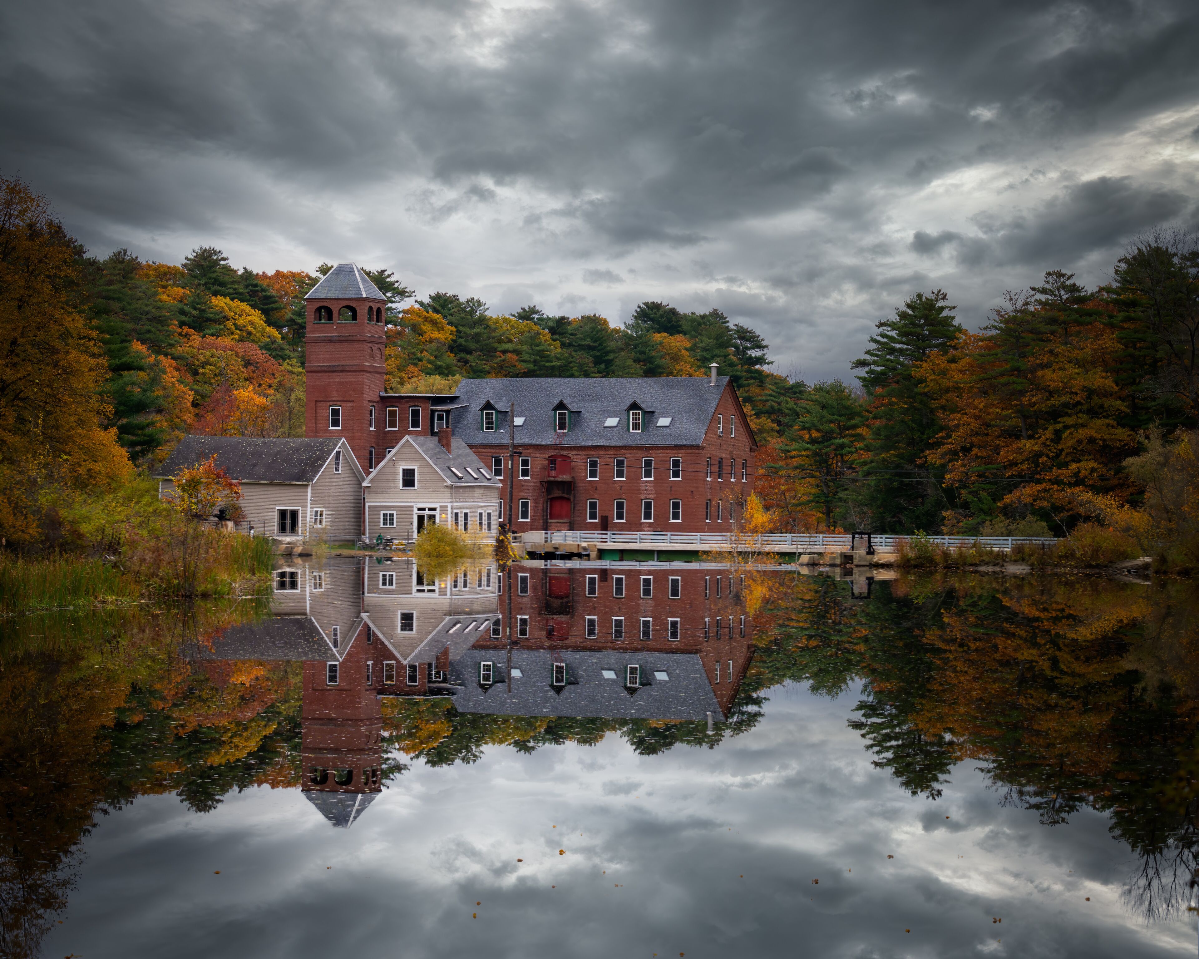 Un edificio histórico con una torre, reflejado en un lago tranquilo rodeado de follaje otoñal.