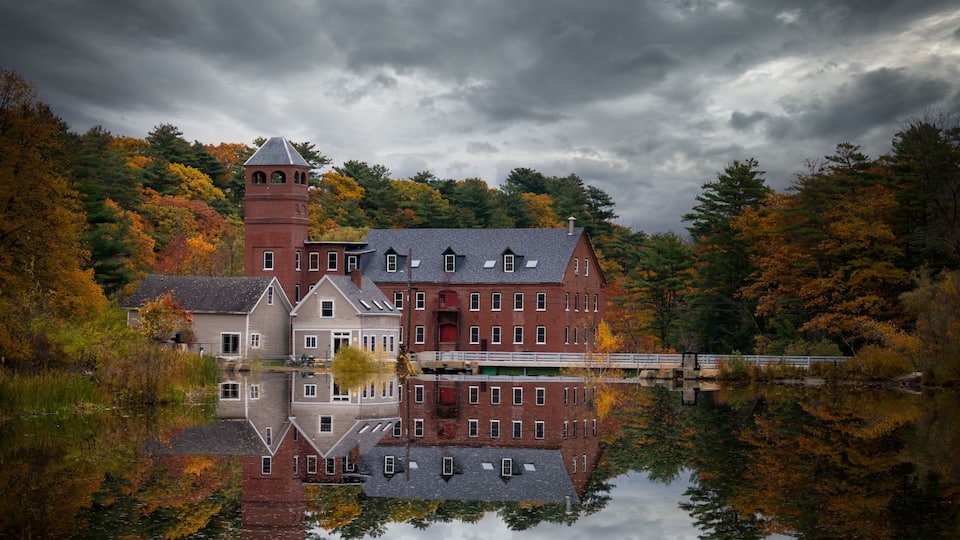 A historic building with a tower, reflecting in a calm lake surrounded by autumn foliage.