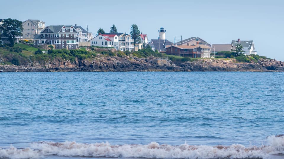 A coastal town with houses, a lighthouse, and a rocky shoreline.