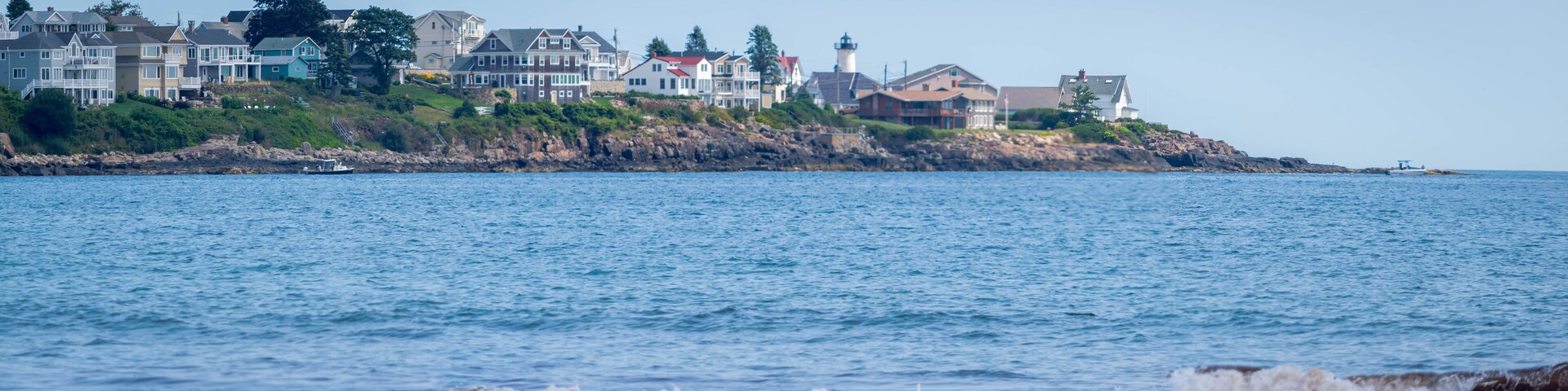 Un pueblo costero con casas, un faro y un litoral rocoso.