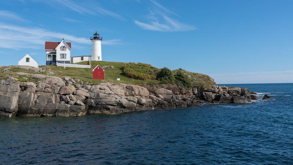 A lighthouse on a rocky cliff with a white building and a red shed.