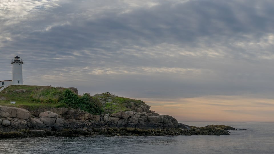 A lighthouse on a rocky outcrop with a cloudy sky.