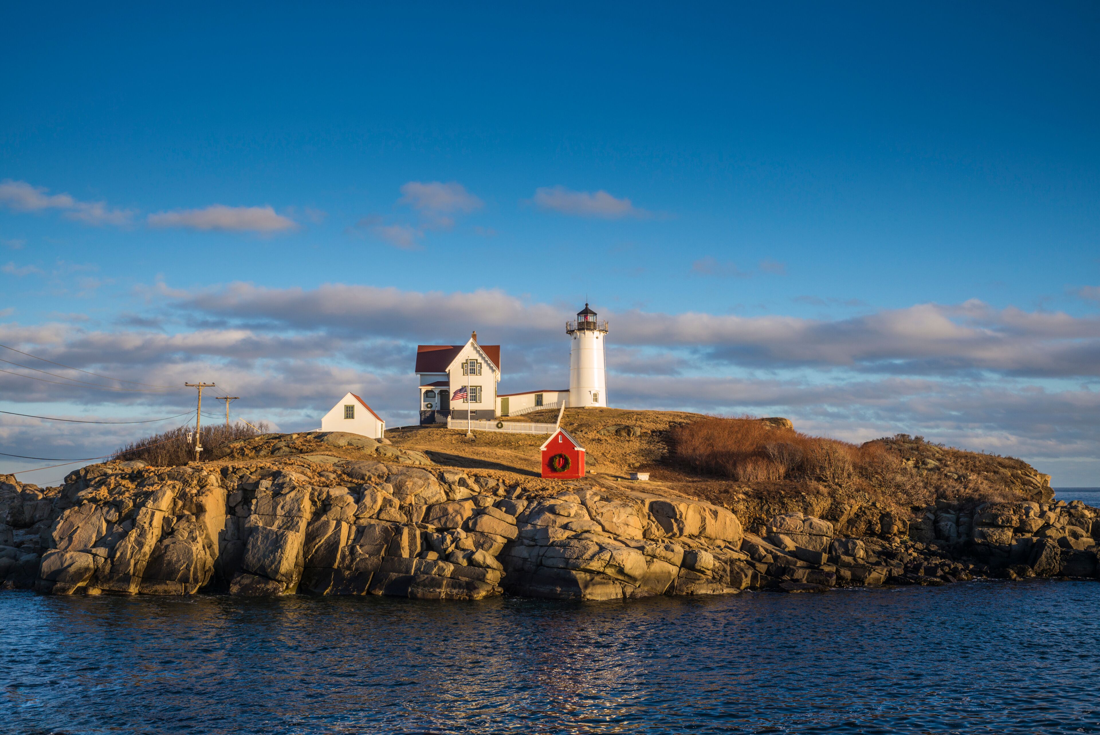 A lighthouse on a rocky island with a white building and a red structure.