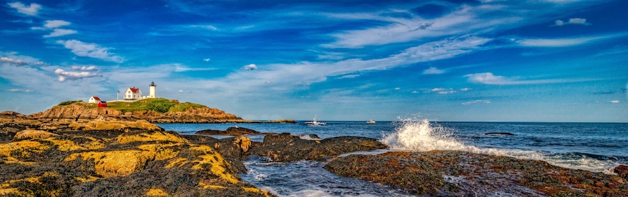 Ein Leuchtturm auf einem Felsen mit dem Meer im Hintergrund.