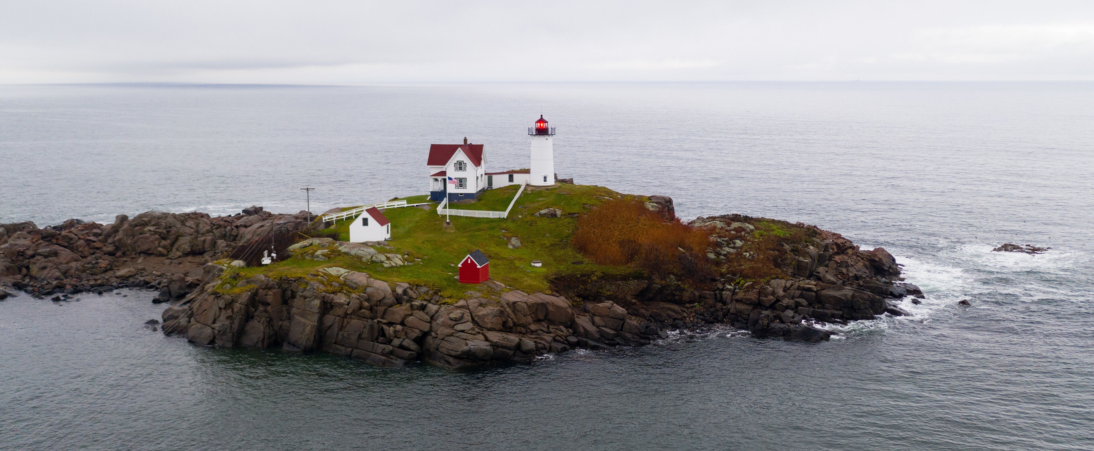 Un phare se dresse sur une île rocheuse, à proximité d’un bâtiment blanc.