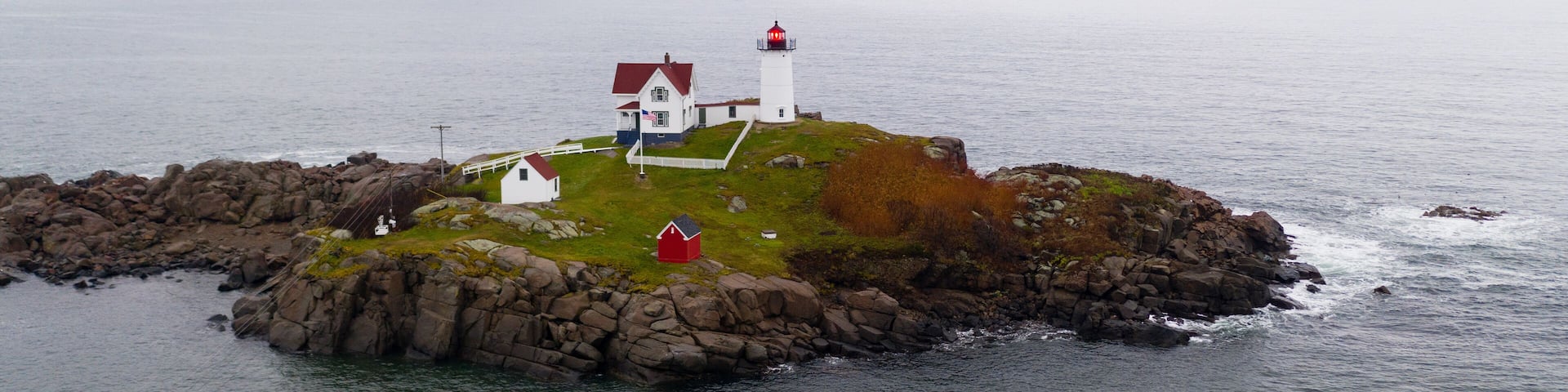 A lighthouse on a rocky island with a white building nearby.