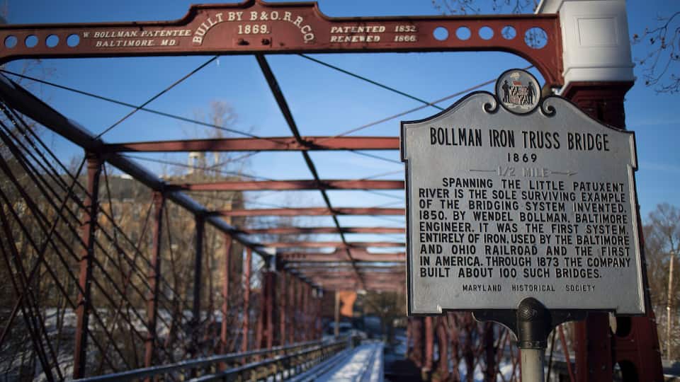 A historical sign for the Bollman Iron Truss Bridge, built in 1869, with details about its significance and construction.