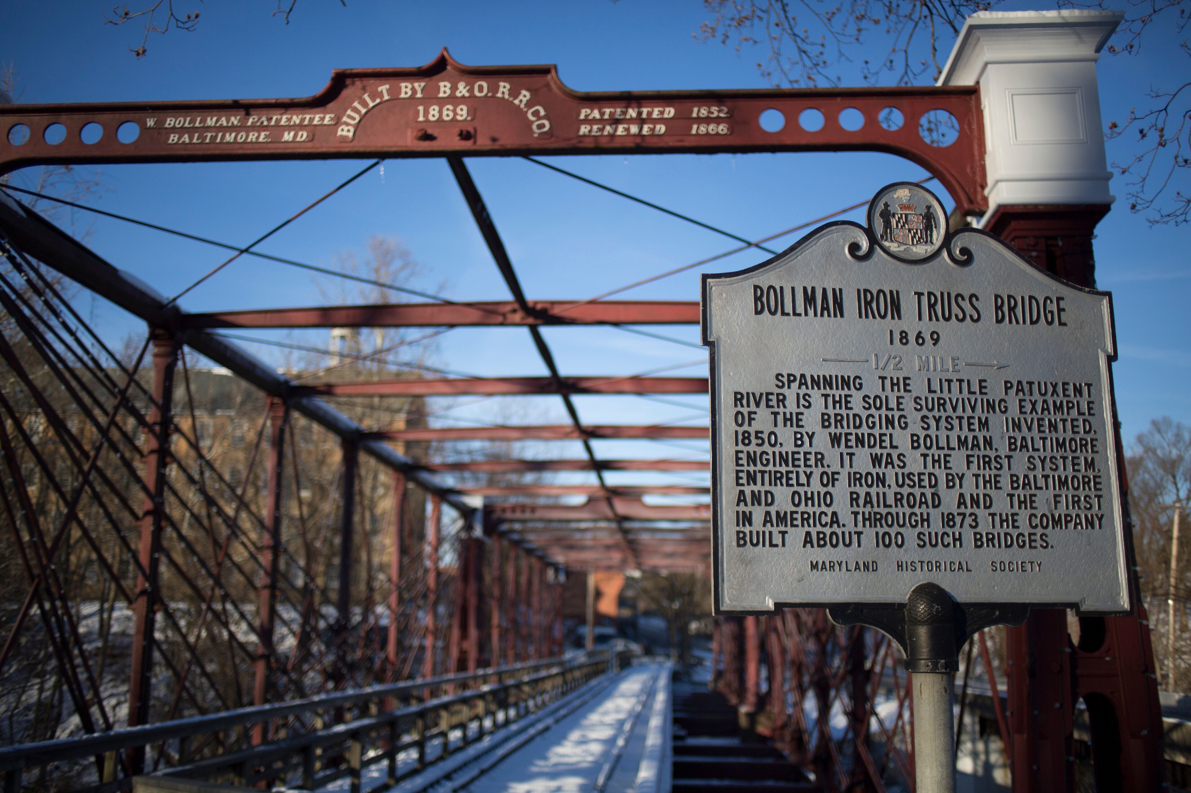 A historical sign for the Bollman Iron Truss Bridge, built in 1869, with details about its significance and construction.