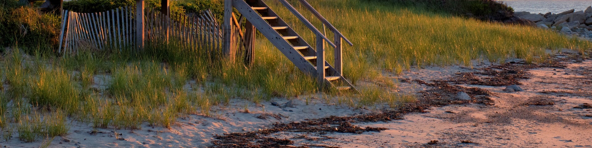 Lovely Cape Cod beach scene with colorful sunlit clouds and sun about to drop below the horizon. Vibrant summer sunset captured at Corporation Beach in Dennis, Massachusetts.