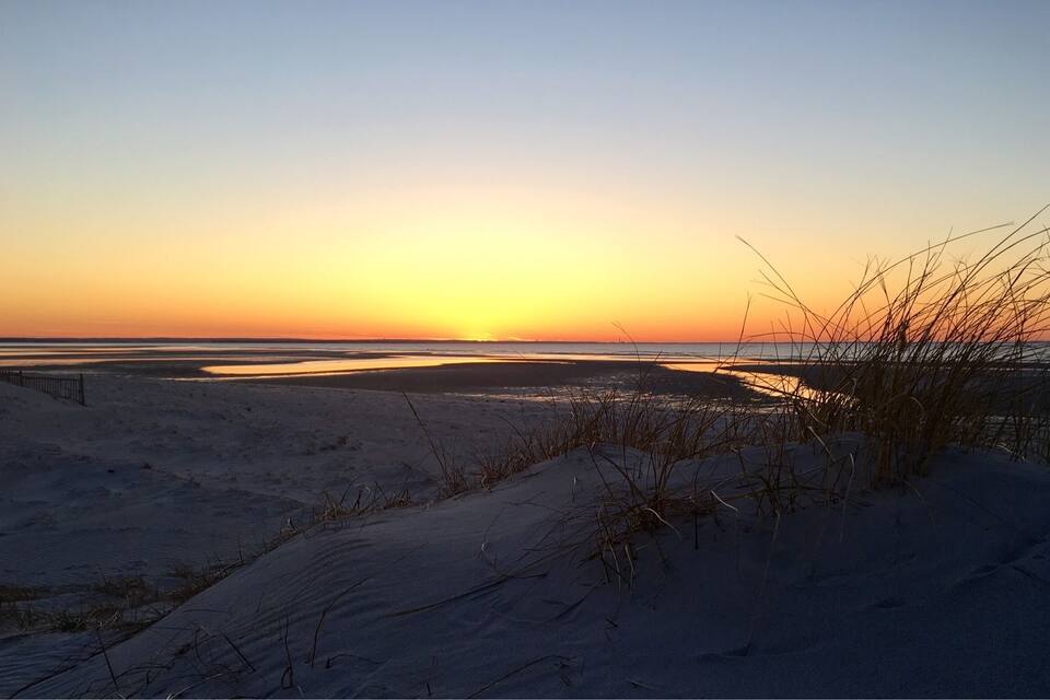Ein Sonnenuntergang über einem verschneiten Strand mit Dünen und Gräsern.