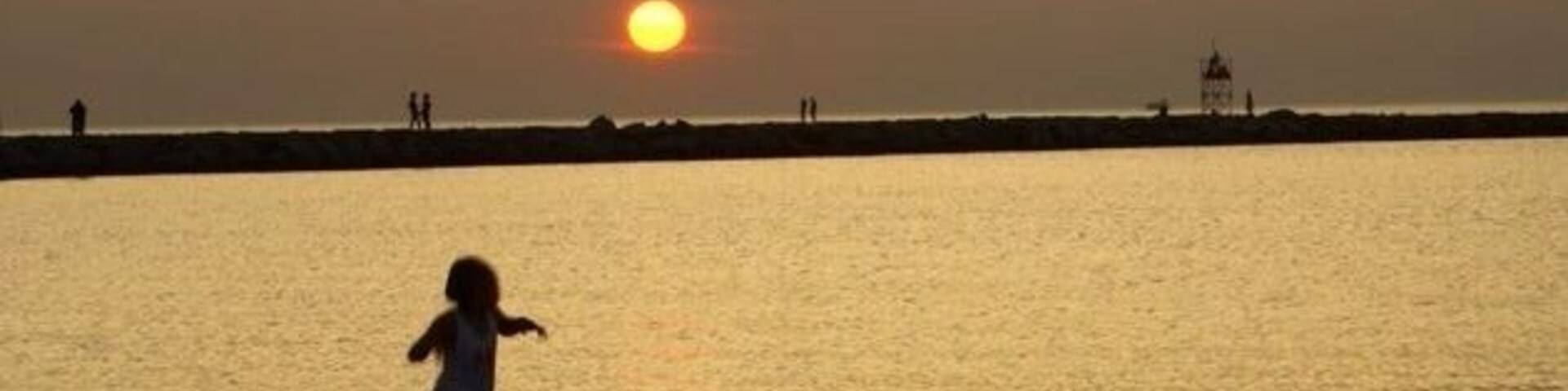 Un atardecer sobre una playa con un niño jugando en el agua.