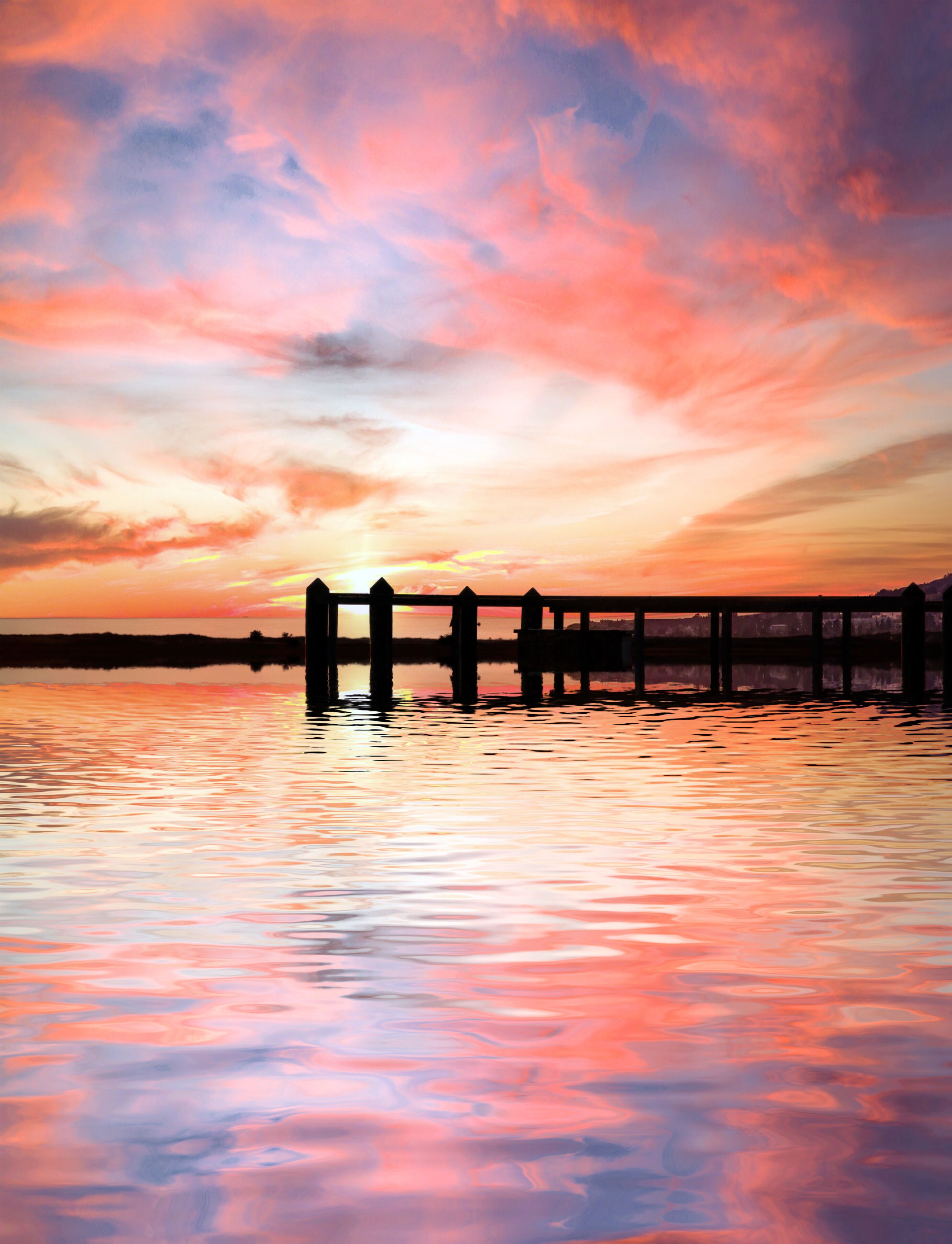 Atardecer sobre una masa de agua tranquila con un muelle de madera que se adentra en ella.