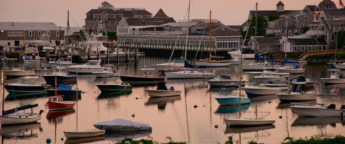 A marina with various boats docked, surrounded by houses and a pier extending into the water.