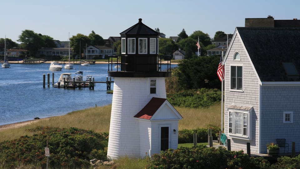 A lighthouse, a white house, and a body of water with boats.