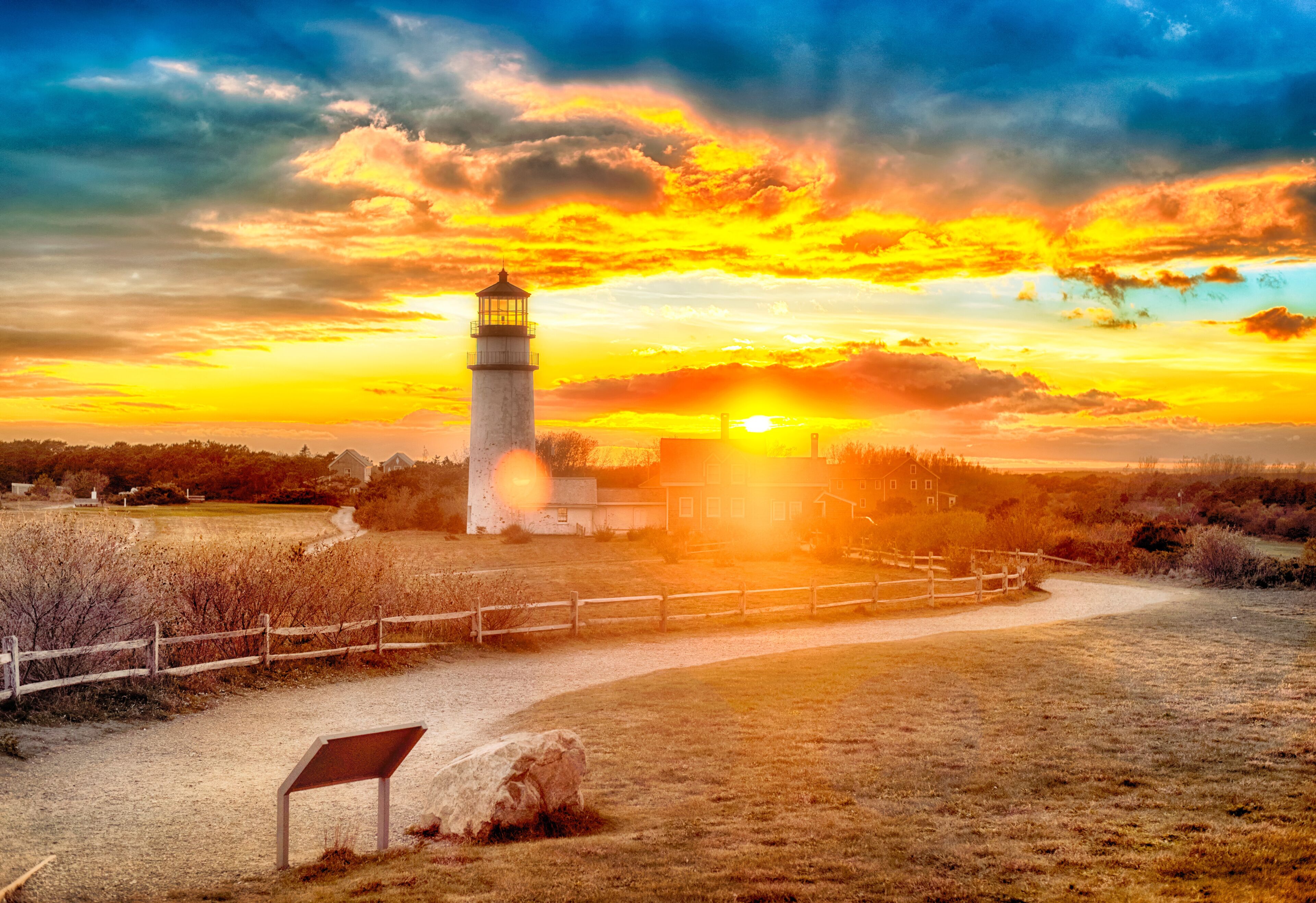 A lighthouse at sunset with a wooden fence and a sign in the foreground.
