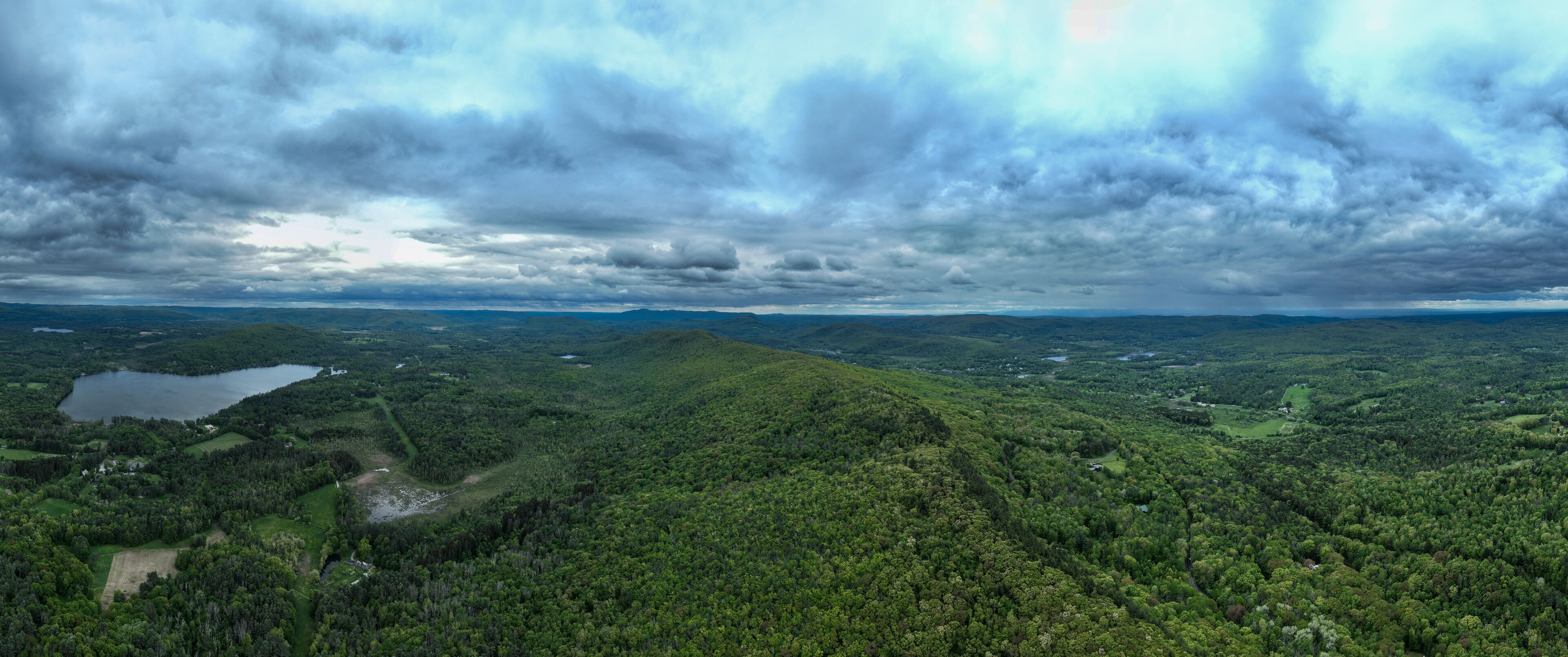 A lush green landscape with a lake and rolling hills under a cloudy sky.