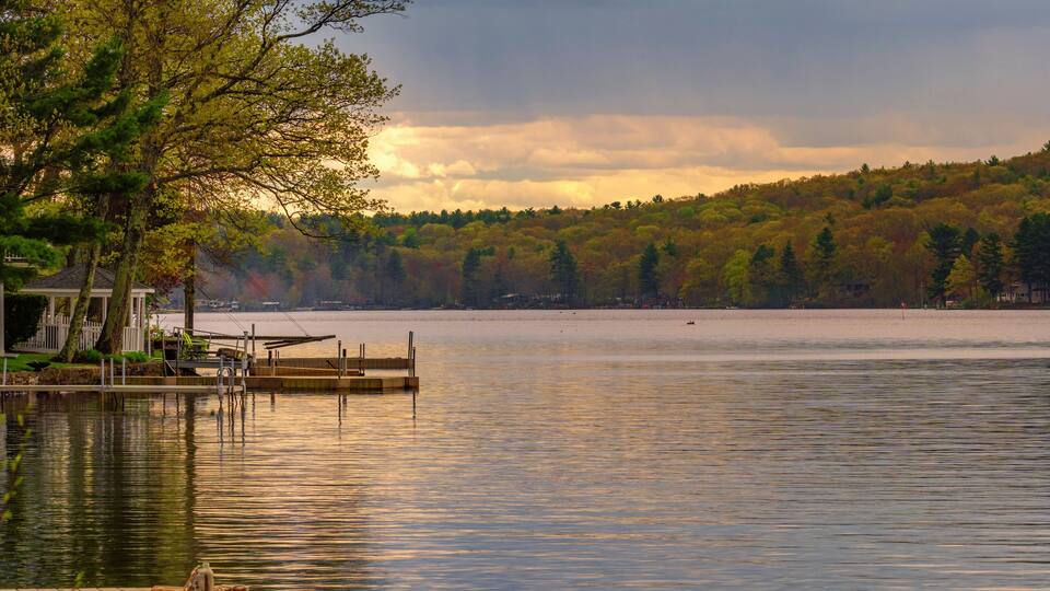 A calm lake with a dock, surrounded by trees and a forested hillside.