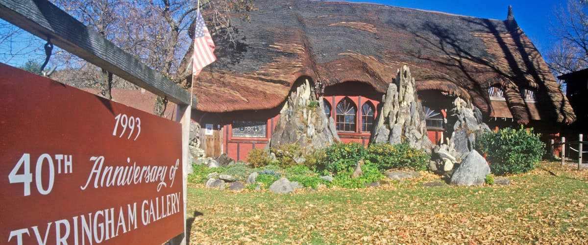 A sign for the 40th anniversary of Tyringham Gallery, a building with a unique thatched roof and stone structures.