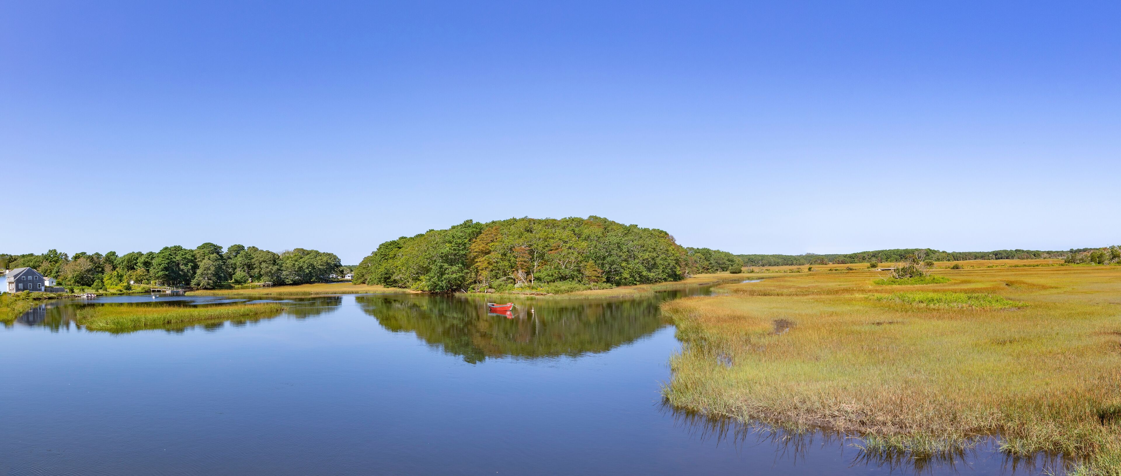 A calm lake with a small red boat, surrounded by lush greenery and a large tree-covered island.