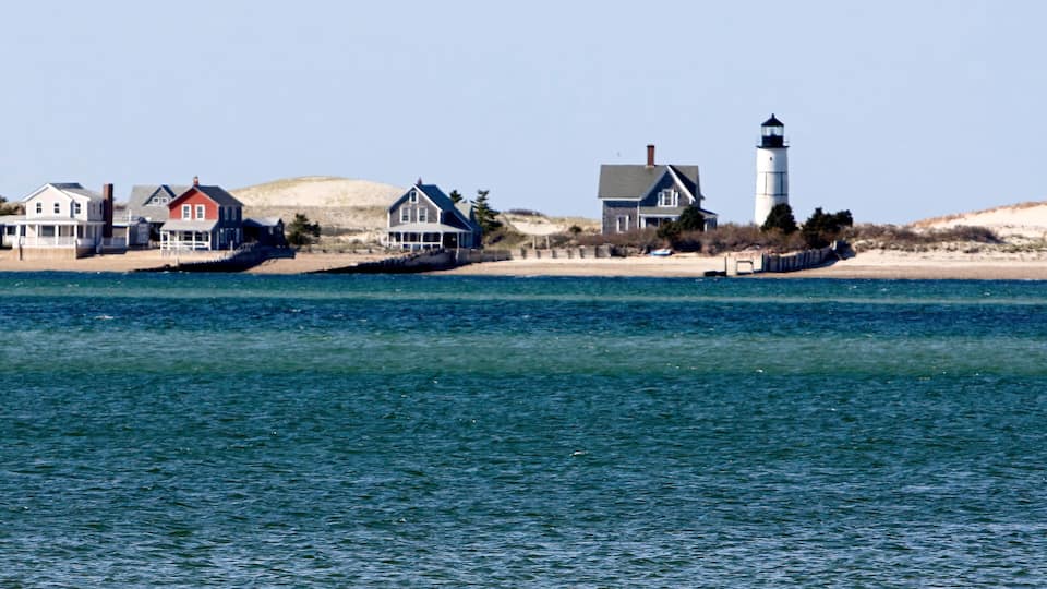 A coastal scene with houses, a lighthouse, and a sandy beach.