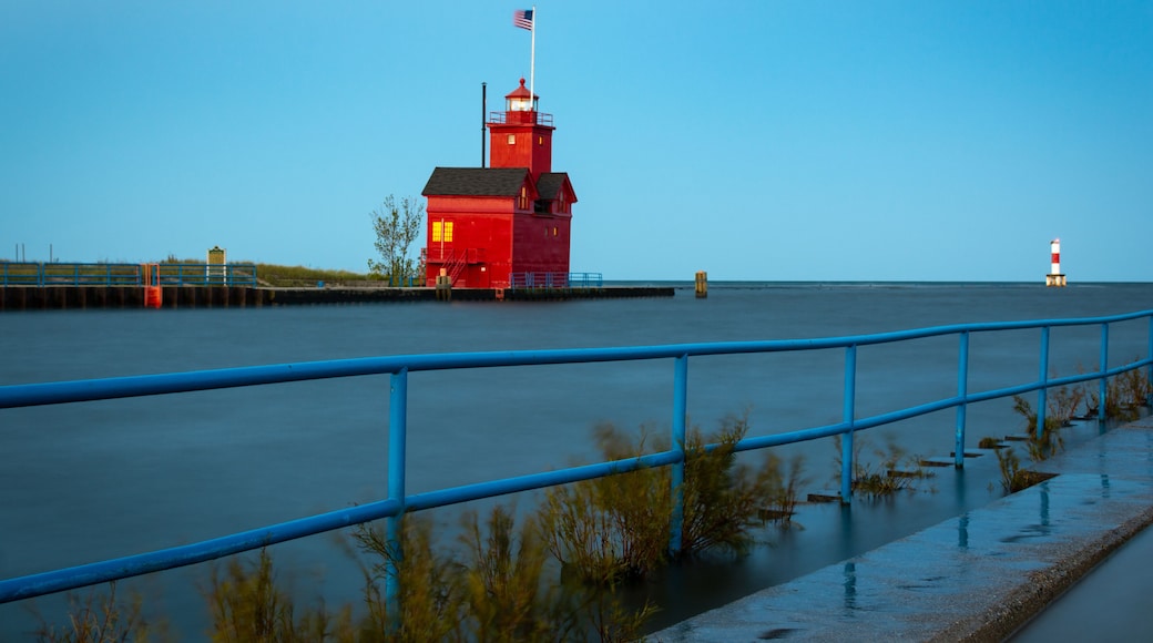 A red lighthouse with a flag, a blue railing, and calm water.