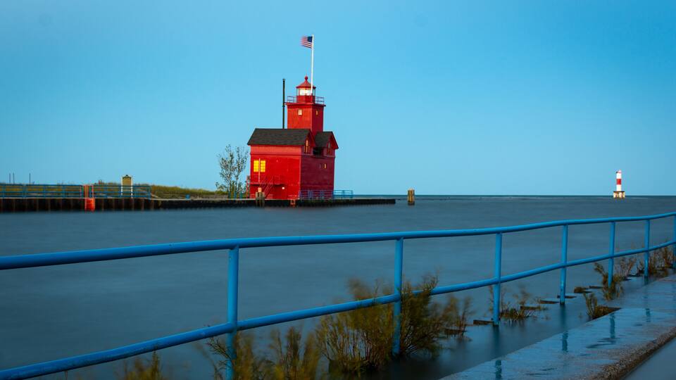 A red lighthouse with a flag, a blue railing, and calm water.