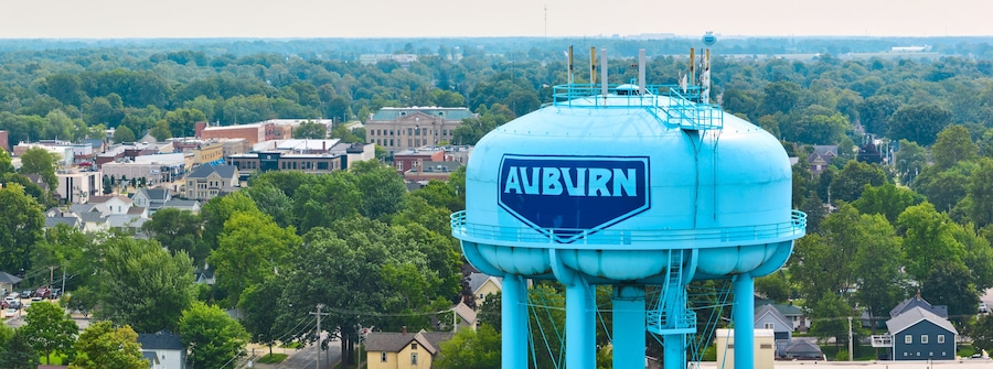 A large water tower with 'Auburn' written on it, surrounded by a cityscape with various buildings and trees.