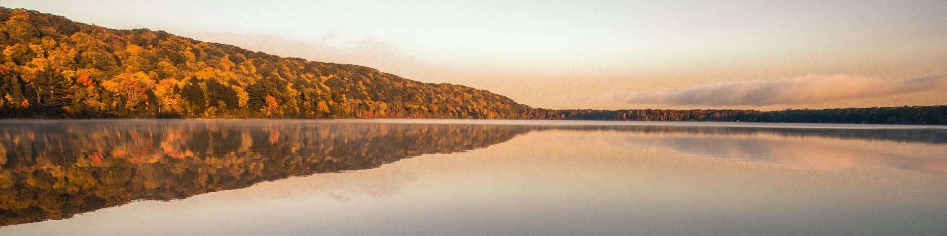 Wilderness Lake Reflections. Monocle Lake in northern Michigan with autumn foliage reflected in the calm blue water of the lake and a sunset horizon. Hiawatha National Forest, Brimley, Michigan.