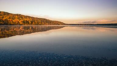 Wilderness Lake Reflections. Monocle Lake in northern Michigan with autumn foliage reflected in the calm blue water of the lake and a sunset horizon. Hiawatha National Forest, Brimley, Michigan.
