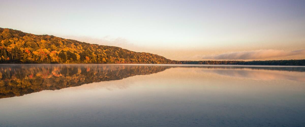A calm lake with a forested hillside in autumn colors.