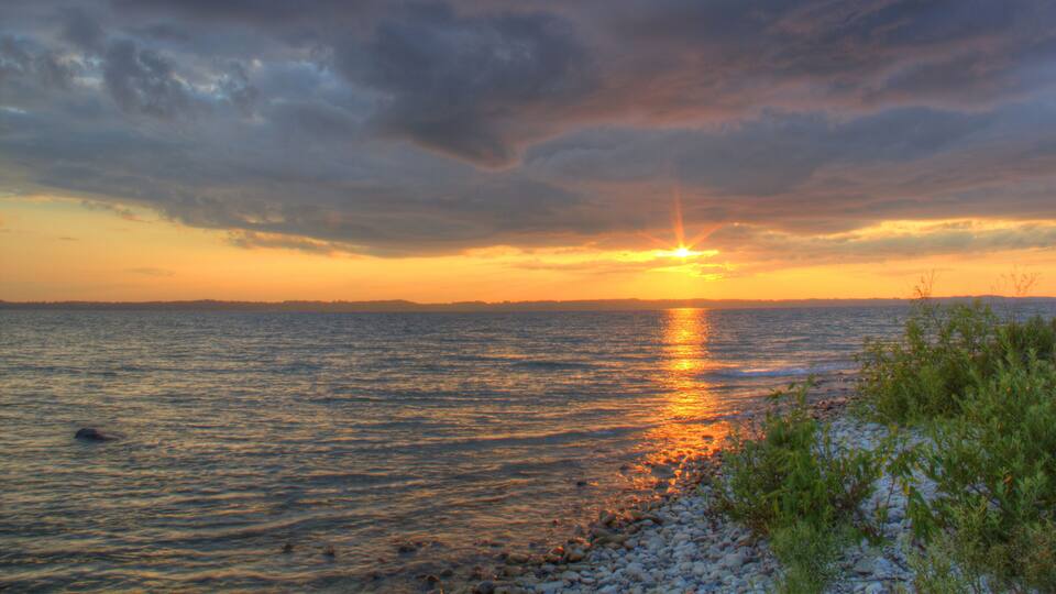 A sunset over a calm sea with rocky shoreline and distant land.