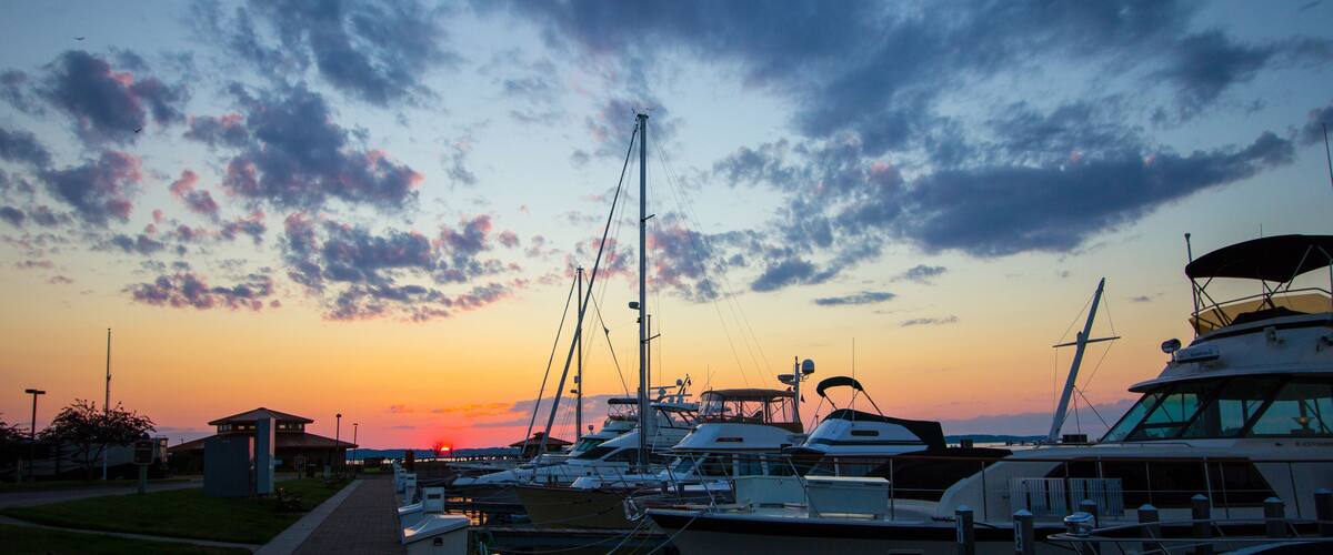 A marina at sunset with boats docked and a clear sky.