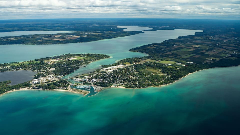 An aerial view of a coastal area with a mix of residential and commercial buildings, surrounded by water bodies and green landscapes.