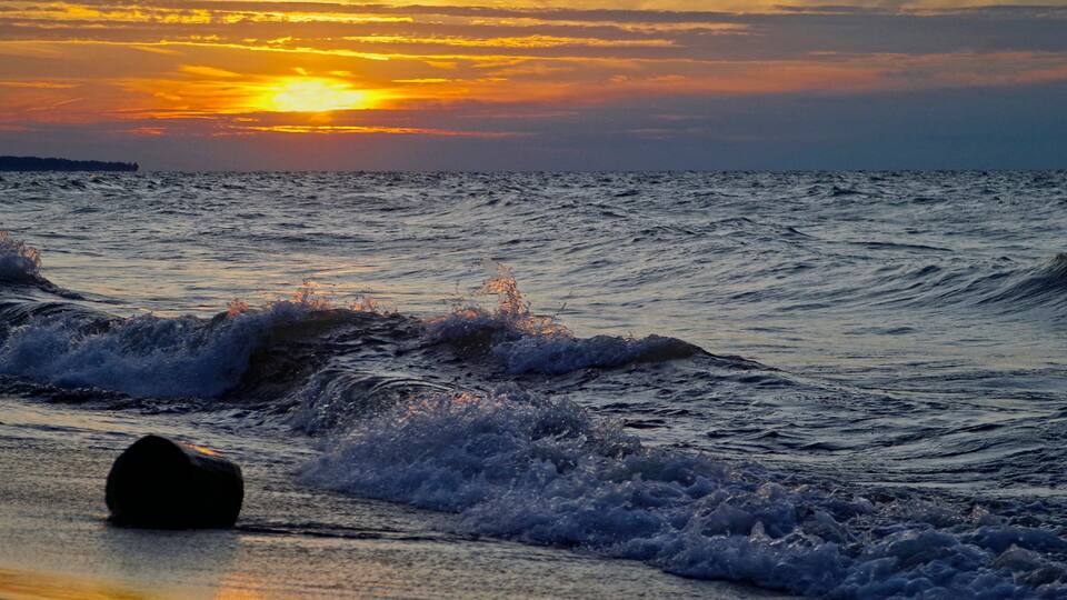 A sunset over the ocean with waves crashing onto the shore.