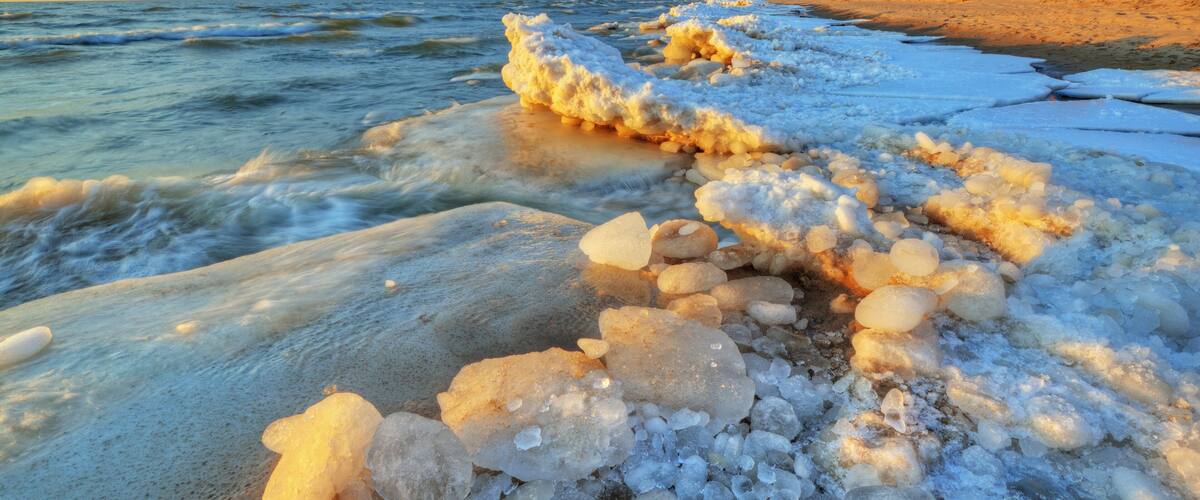 A frozen shoreline with ice formations and a distant forested hill.