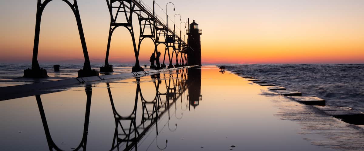 A pier extending into the sea with a sunset in the background.